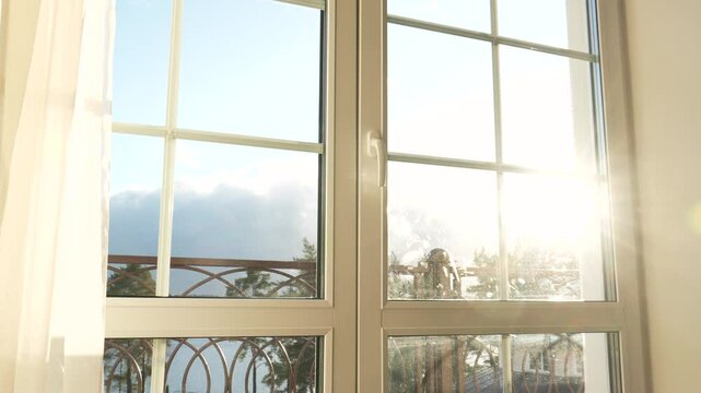 Bright sunlight streaming through windows in room, illuminating balcony with expansive lake and verdant treetops landscape. Morning dawn and meeting of new day. Warm rays enter the house at sunset