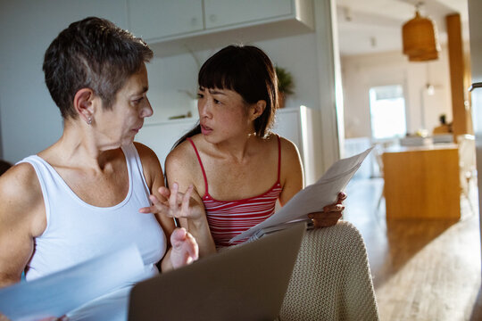 Lesbian couple handling bills at home with laptop