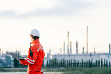 Industrial professional in safety attire analyzing refinery operations using modern technology, showcasing leadership and expertise in industrial safety and infrastructure projects.