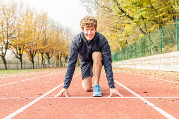 Obraz premium Close up of male runner sprinting on red track lane at outdoor stadium during training session. Male in sportswear and blue sneakers ready to run. Healthy lifestyle and outdoor sport concepts. 
