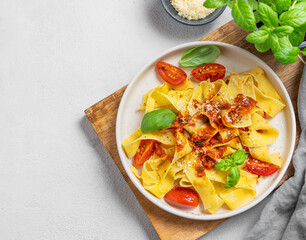 Homamade tagliatelle pasta with tomato sauce, basil and parmesan cheese in a plate on a wooden board on a light background