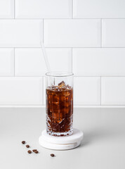 Cold brew coffee in a glass with ice on a light table against a white brick background