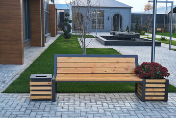 Wooden bench with a metal frame, next to a trash can and a flower pot with red flowers, all in a...