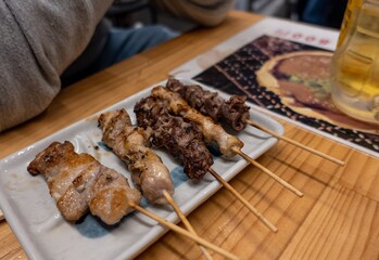 Meat skewers on a wooden table beside a glass of beer. Japan
