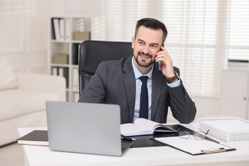 Happy banker talking on smartphone at table in office