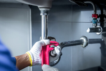 Plumber hands holding wrench doing repairing work at the sink and clogged pipe in bathroom carefully