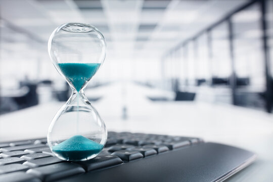 Hourglass on top of computer keyboard on desk in large office concept for time management and schedule