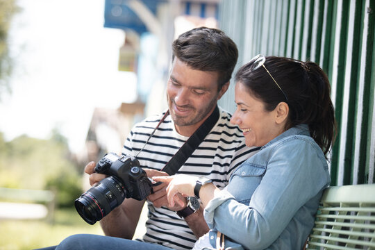 couple of tourists reviewing photos on camera sitting on bench