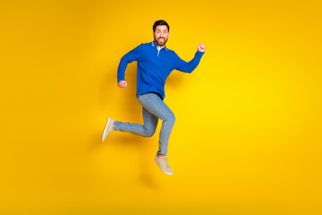 Full body photo of attractive young man fast running excited dressed stylish blue clothes isolated on yellow color background