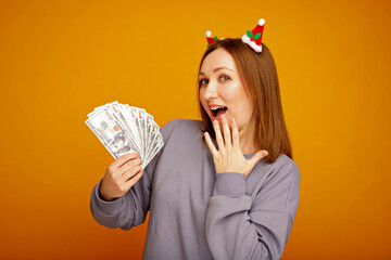 Woman wearing christmas headband holding one hundred dollar bills on yellow background