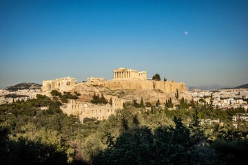 The acropolis in Athens is beautifully surrounded by trees and day moon. Greece
