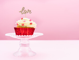 Valentine's Day. A cupcake with cream and red topping decoration with a wooden sign with the word LOVE on a pink background. Pastry bakery.