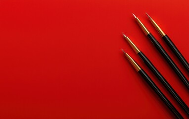 Four paintbrushes with golden tips are arranged on a bold red background, highlighting their elegance and artistic potential.