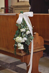 Elegant wedding pew decoration featuring white roses, eucalyptus leaves, and a flowing white...