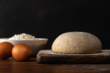 Fresh raw dough for bread or pizza with eggs on a dark wooden table.