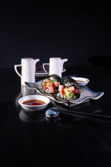 Plato de Temakis con salsa de soya en fondo negro,  sushi de salm&oacute;n. Comida Japonesa.