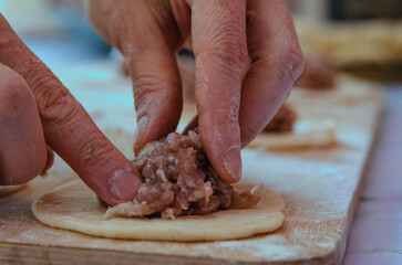 Chef's hands fingers close-up making dumplings from dough and meat. 