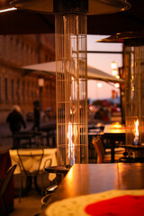 In the European city, an outdoor gas heater with a flame inside is installed in the open area of ​​a restaurant.