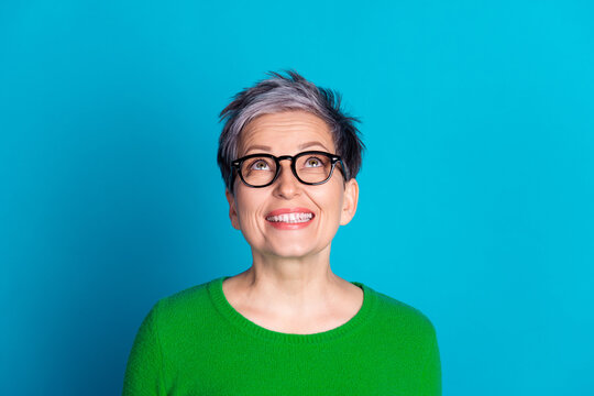 Elderly woman with glasses smiling happily against vibrant blue background in a joyful and dynamic portrait.
