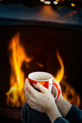 A female hand holding a cup of coffee near a fireplace