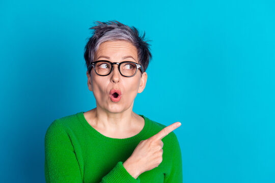 Surprised mature woman with gray hair pointing sideways against bright blue background