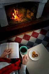 A female hand holding a cup of coffee near a fireplace