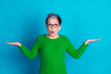 Surprised mature woman in green sweater against a vibrant blue background, expressing wonder with...