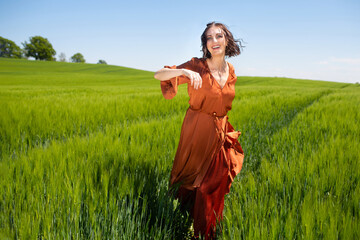 Obraz premium Joyful young caucasian woman in orange dress running through lush green field