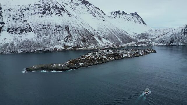 Aerial view of a fishing boat sailing back to the harbor in Husoy, a fishing village in Norway, winter time