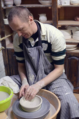 Young man in apron sitting in workshop and working with clay