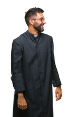 Adult hispanic catholic priest man over isolated background looking away to side with smile on...