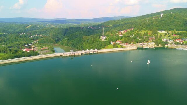 Panoramic view of Solina Lake and dam with a sailboat and vibrant natural surroundings.