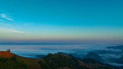 A breathtaking aerial view of a mist-covered forest at sunrise. The dramatic cloudscape and soft fog create a serene and mystical atmosphere. Misty Sunrise Over Forested Hills with layers of mountain