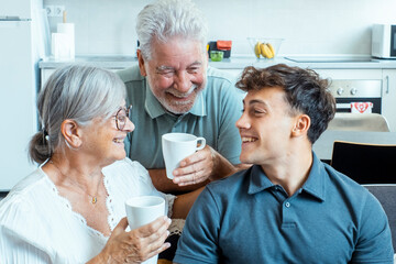 Family at home during a festive evening with grandparents and grandson enjoying tea together while sitting on the couch, sharing stories, smiling, laughing, and creating a cheerful and cozy 