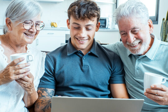 Elderly grandmother and young grandson sitting comfortably on a sofa in the living room, enjoying tea, smiling, laughing, and bonding while sharing cheerful stories during a festive family gathering