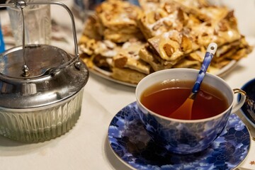 Porcelain teacup with spoon and metal kettle near plate of cake on table