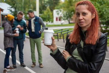 Ginger girl in black leather jacket outdoors holding a cup of coffee, looking at camera