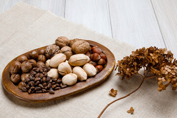 Variety of nuts and coffee beans arranged on a wooden platter with dried flowers on a textured surface