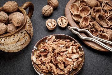 Various types of nuts arranged on a dark surface with tools and shells nearby for shelling