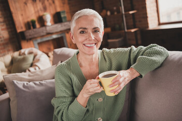Charming senior woman enjoying a relaxed weekend at home with a warm drink in stylish green sweater