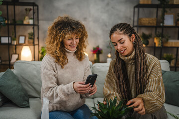 female friends photographing flower pot with mobile phone at home
