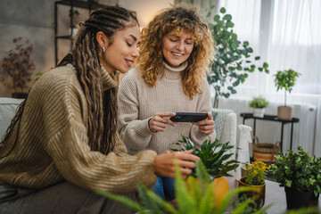 female friends photographing flower pot with mobile phone at home