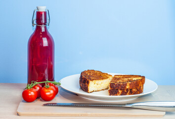 A grilled tiger bread cheese sandwich on a plate and a sustainable bamboo chopping board with water bottle or coffee. Side of tomatoes on the vine