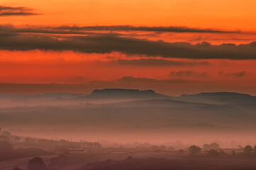Dorset Sunrise with a beautiful red and orange coloured sky over the distant hills with mist and fog in the valley