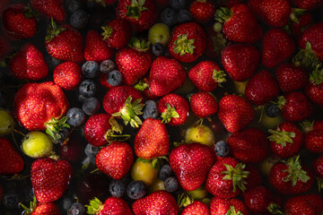 Fresh strawberries, blueberries, and green plums floating in water, illuminated by natural light. Vibrant and colorful assortment of summer fruits, perfect for healthy eating and refreshing beverages