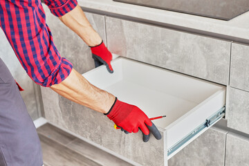 Repairman Repairing Cabinet Hinge In Kitchen. Help for People in New House. Male hand adjusting a...