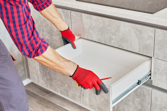 Repairman Repairing Cabinet Hinge In Kitchen. Help for People in New House. Male hand adjusting a mechanism. Professional furniture worker assembling kitchen closets.