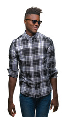 Fototapeta premium Young african american man wearing sunglasses over isolated background looking away to side with smile on face, natural expression. Laughing confident.