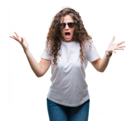 Beautiful brunette curly hair young girl wearing sunglasses over isolated background celebrating mad and crazy for success with arms raised and closed eyes screaming excited. Winner concept