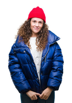 Beautiful young brunette curly hair girl wearing winter coat, wool cap and sweater over isolated background with a happy and cool smile on face. Lucky person.